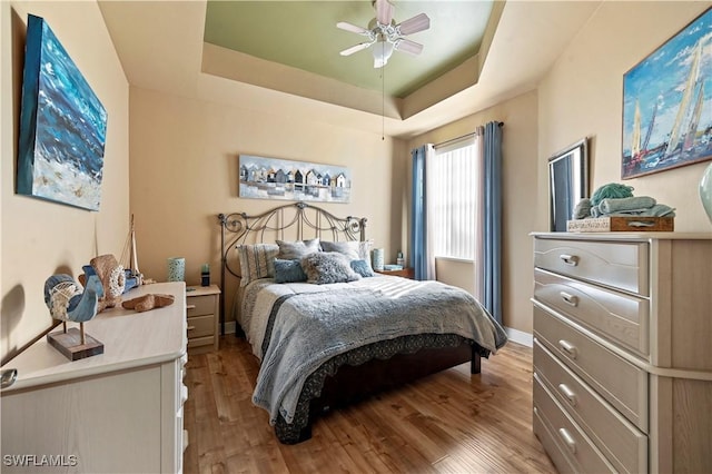 bedroom featuring baseboards, a tray ceiling, a ceiling fan, and light wood-style floors