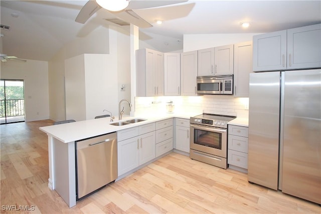 kitchen with lofted ceiling, sink, appliances with stainless steel finishes, light hardwood / wood-style floors, and kitchen peninsula