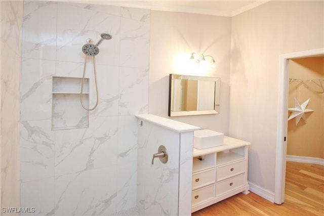 bathroom featuring hardwood / wood-style floors, vanity, a tile shower, and crown molding