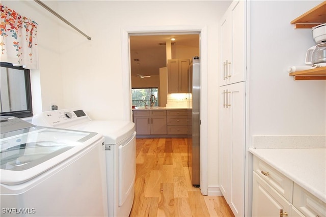 laundry area with cabinets, light wood-type flooring, sink, and washing machine and clothes dryer