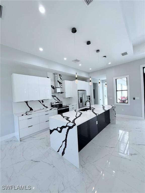 kitchen featuring white cabinets, a large island with sink, decorative light fixtures, and appliances with stainless steel finishes