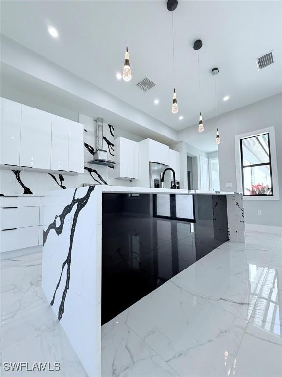 kitchen featuring white cabinets, light stone counters, stainless steel fridge with ice dispenser, and hanging light fixtures