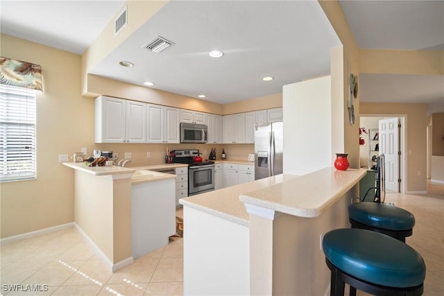 kitchen with a breakfast bar, white cabinetry, light tile patterned floors, appliances with stainless steel finishes, and kitchen peninsula