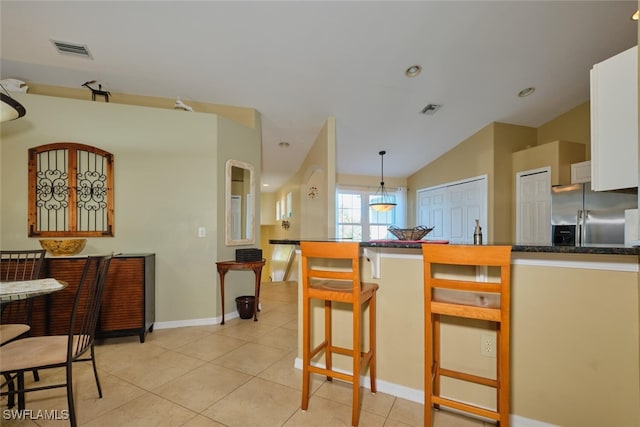 kitchen featuring white cabinetry, stainless steel fridge with ice dispenser, vaulted ceiling, a breakfast bar area, and light tile patterned flooring