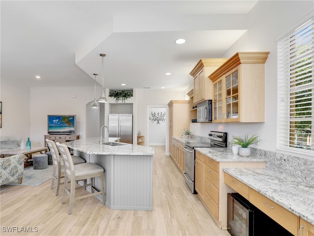 kitchen featuring a center island with sink, light stone countertops, appliances with stainless steel finishes, a breakfast bar area, and light brown cabinetry