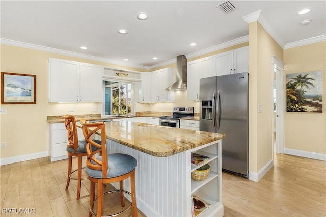 kitchen with light wood-type flooring, wall chimney exhaust hood, stainless steel appliances, white cabinetry, and a kitchen island