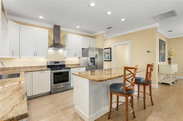 kitchen with appliances with stainless steel finishes, light stone counters, wall chimney exhaust hood, white cabinets, and light hardwood / wood-style floors