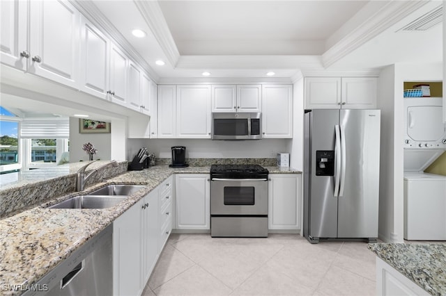 kitchen featuring white cabinets, a raised ceiling, stacked washer and dryer, and appliances with stainless steel finishes