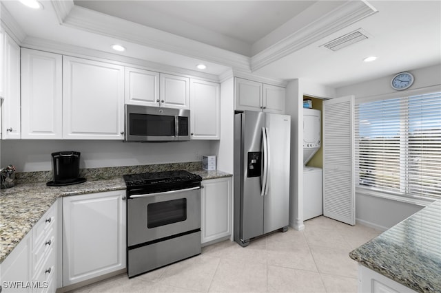 kitchen with a tray ceiling, stacked washer / dryer, white cabinets, and appliances with stainless steel finishes