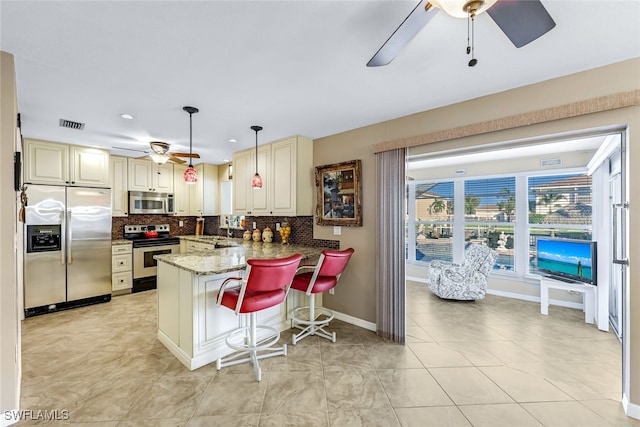 kitchen featuring stainless steel appliances, a kitchen breakfast bar, kitchen peninsula, dark stone counters, and decorative light fixtures