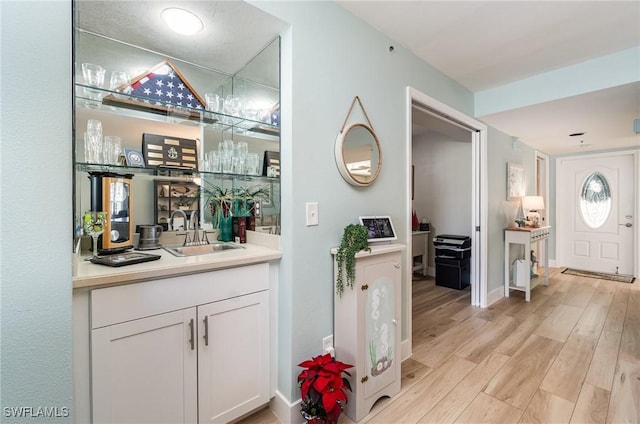 bar with white cabinets, light hardwood / wood-style floors, and sink