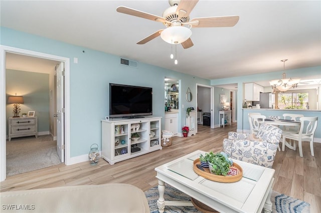 living room with light hardwood / wood-style floors and ceiling fan with notable chandelier