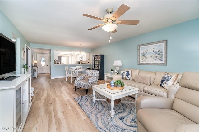 living room featuring ceiling fan with notable chandelier, light wood-type flooring, and vaulted ceiling