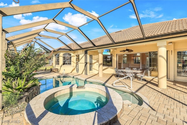 view of swimming pool with glass enclosure, ceiling fan, a patio, and an in ground hot tub