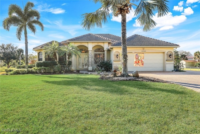 mediterranean / spanish house featuring decorative driveway, a tile roof, stucco siding, an attached garage, and a front yard