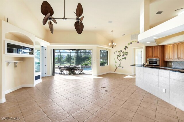 unfurnished living room with ceiling fan with notable chandelier, light tile patterned flooring, and high vaulted ceiling