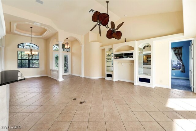 unfurnished living room featuring a raised ceiling, ornate columns, light tile patterned floors, and ceiling fan with notable chandelier