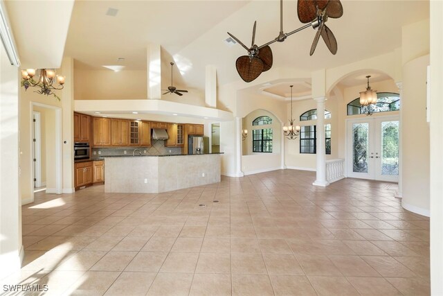 unfurnished living room with french doors, ceiling fan with notable chandelier, sink, light tile patterned floors, and high vaulted ceiling