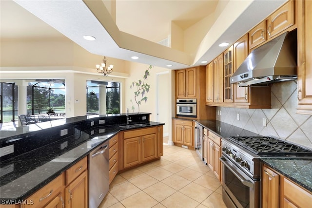 kitchen with dark stone counters, stainless steel appliances, sink, exhaust hood, and an inviting chandelier