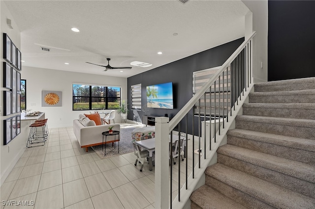 staircase with ceiling fan, tile patterned flooring, and a textured ceiling