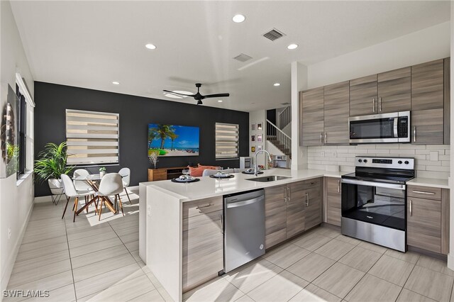 kitchen featuring ceiling fan, sink, stainless steel appliances, tasteful backsplash, and kitchen peninsula