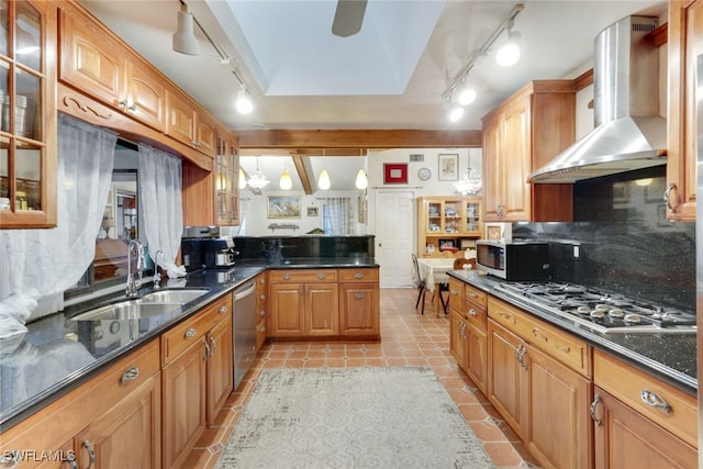 kitchen featuring wall chimney range hood, sink, appliances with stainless steel finishes, decorative light fixtures, and dark stone counters