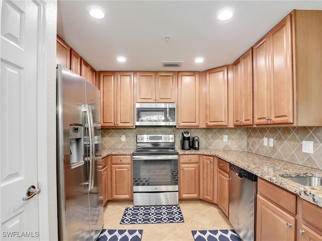 kitchen featuring sink, light stone countertops, tasteful backsplash, light tile patterned flooring, and stainless steel appliances