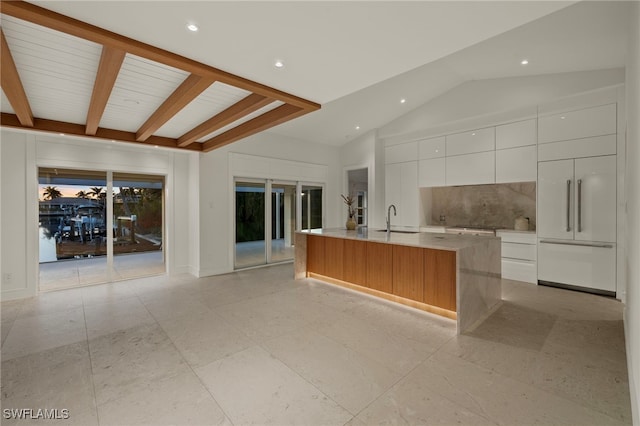 kitchen featuring sink, vaulted ceiling with beams, tasteful backsplash, a large island, and white cabinetry