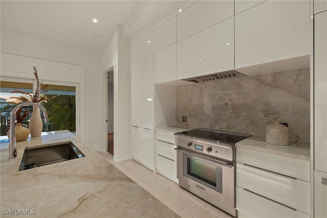 kitchen featuring white cabinetry, sink, high end range, and light stone countertops