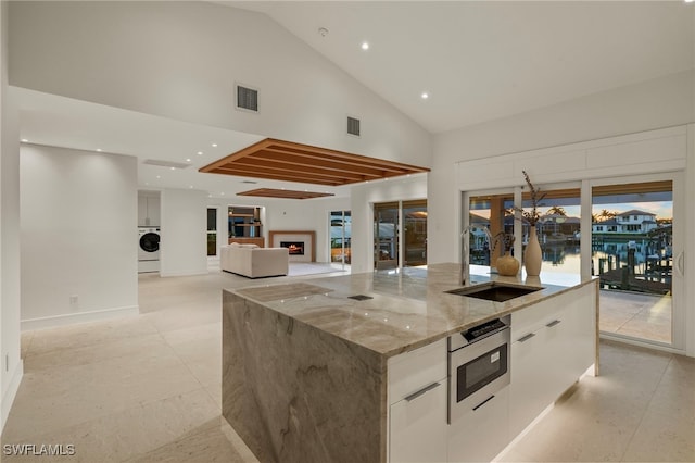 kitchen with high vaulted ceiling, sink, light stone countertops, a large island, and white cabinetry