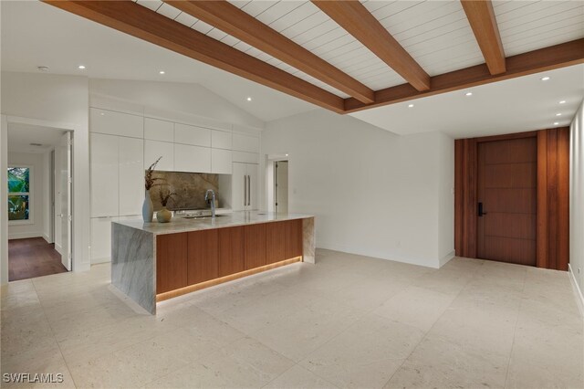 kitchen featuring backsplash, sink, a large island with sink, lofted ceiling with beams, and white cabinetry