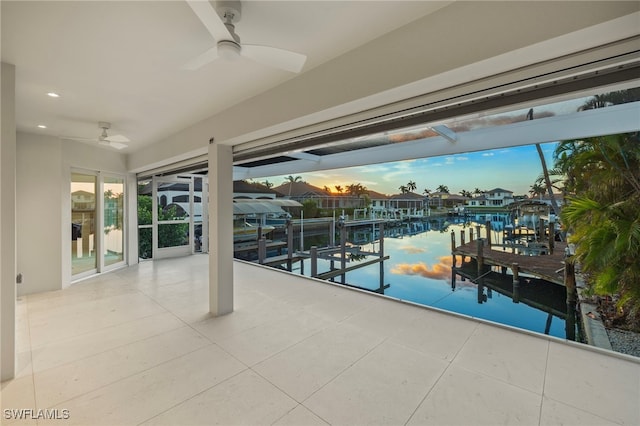 patio terrace at dusk featuring a boat dock, ceiling fan, and a water view