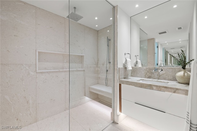 bathroom featuring a tile shower, vanity, tile patterned floors, and tile walls