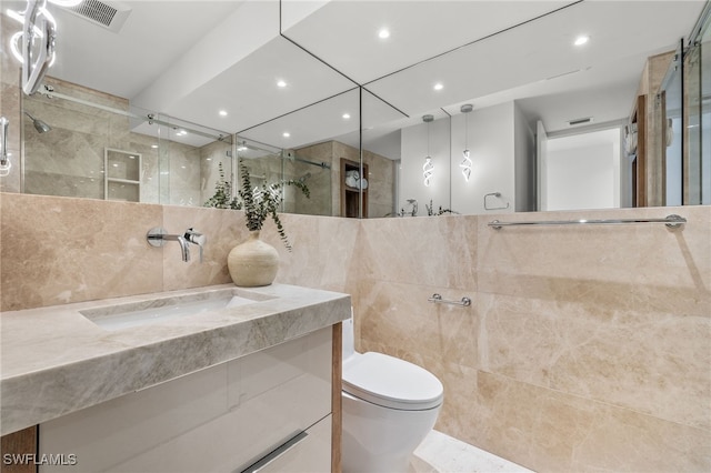 bathroom featuring vanity, toilet, a shower with shower door, and tile walls