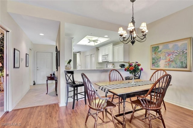 dining room with ceiling fan with notable chandelier, light hardwood / wood-style floors, and a skylight