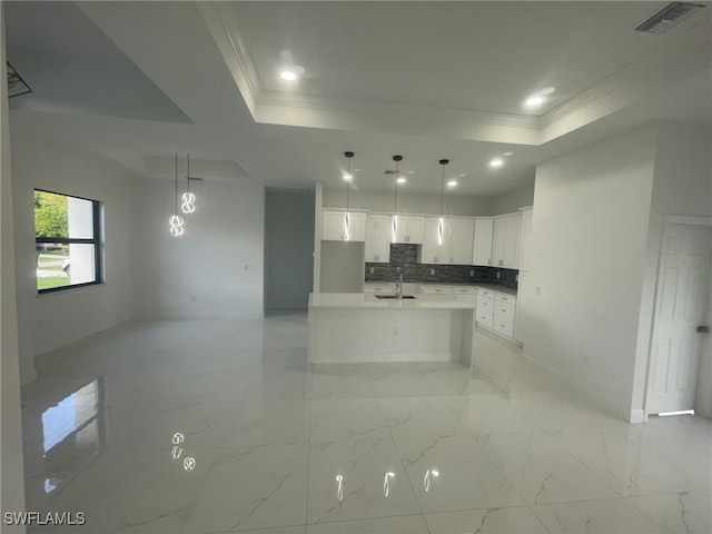 kitchen featuring backsplash, a center island with sink, sink, a tray ceiling, and white cabinetry