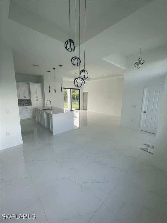 interior space with decorative light fixtures, white cabinetry, sink, and an island with sink