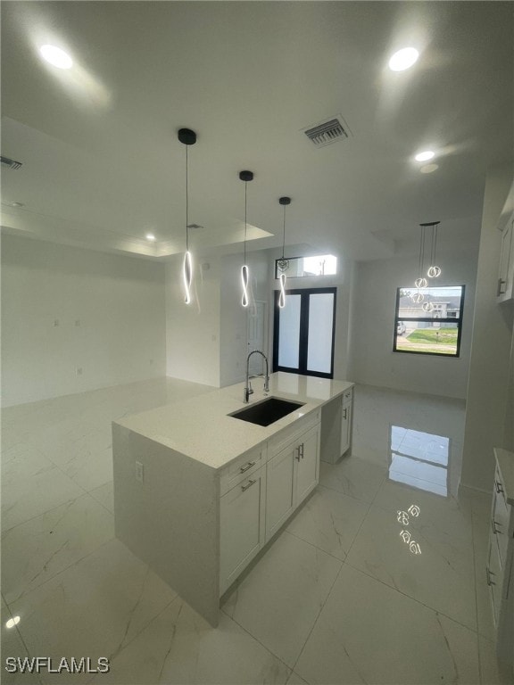 kitchen with sink, white cabinets, decorative light fixtures, and a center island with sink