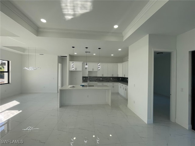 kitchen with crown molding, a tray ceiling, an island with sink, and white cabinets