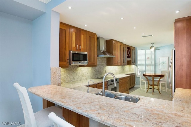 kitchen featuring sink, wall chimney exhaust hood, stainless steel appliances, kitchen peninsula, and a breakfast bar area