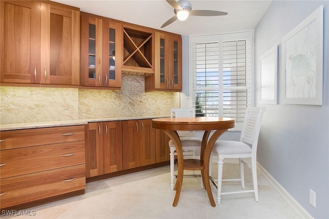 interior space with decorative backsplash, ceiling fan, light tile patterned floors, and light stone counters