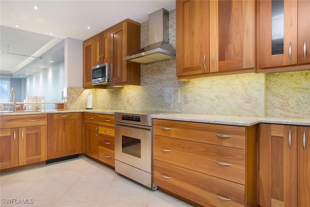 kitchen featuring sink, wall chimney exhaust hood, appliances with stainless steel finishes, tasteful backsplash, and light stone counters