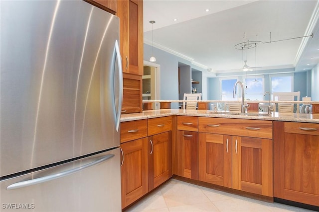 kitchen featuring crown molding, sink, light stone countertops, decorative light fixtures, and stainless steel refrigerator