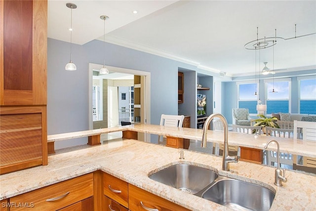 kitchen featuring a water view, sink, crown molding, hanging light fixtures, and light stone counters