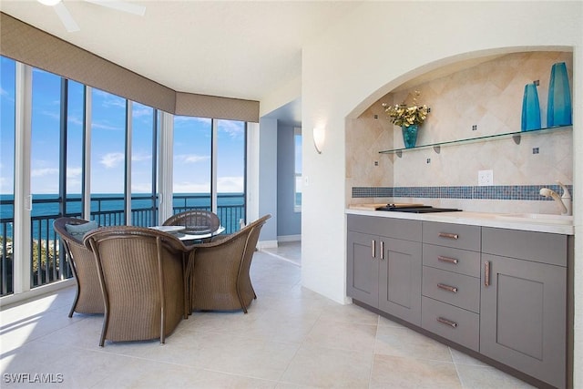 kitchen with sink, light tile patterned floors, gray cabinets, decorative backsplash, and a water view