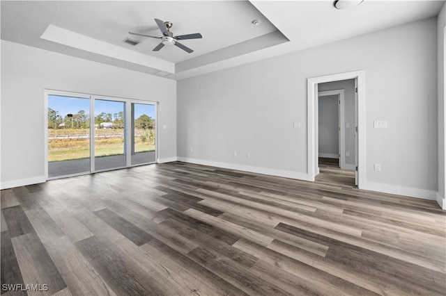 empty room with ceiling fan, wood-type flooring, and a tray ceiling