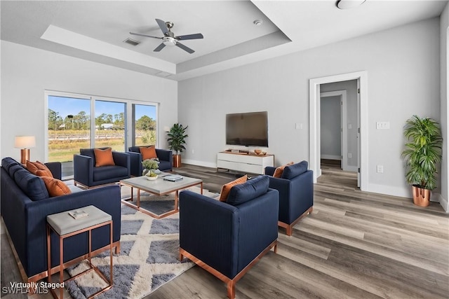 living room featuring ceiling fan, a raised ceiling, and wood-type flooring