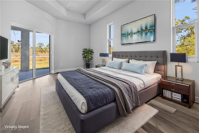 bedroom with light hardwood / wood-style floors, a raised ceiling, and access to outside