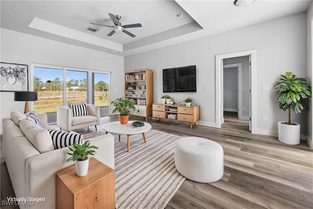 living room featuring ceiling fan, hardwood / wood-style floors, and a tray ceiling