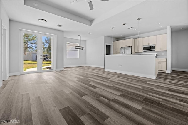 unfurnished living room with dark hardwood / wood-style floors, a tray ceiling, ceiling fan, and french doors